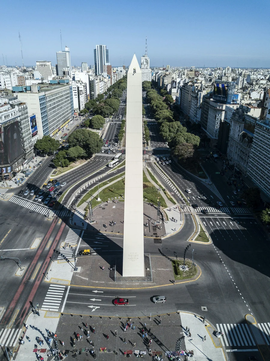 Luftaufnahme des Obelisco über der Avenida 9 de Julio in Buenos Aires mit Straßenverkehr und der Skyline im Hintergrund.