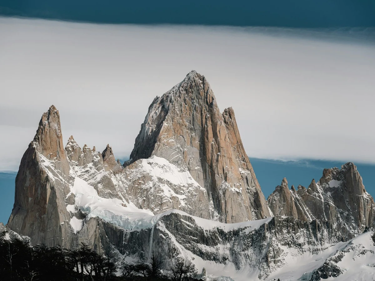 Schneebedeckte Granitspitzen des Fitz-Roy-Massivs unter einem breiten Wolkenband in Patagonien.
