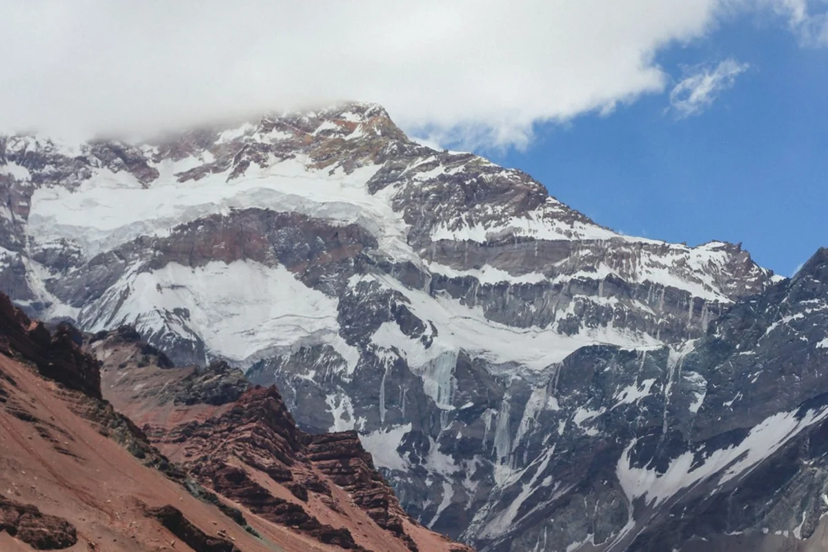 Schnee und Eis an steilen Felswänden des Aconcagua über rötlichem Gestein.
